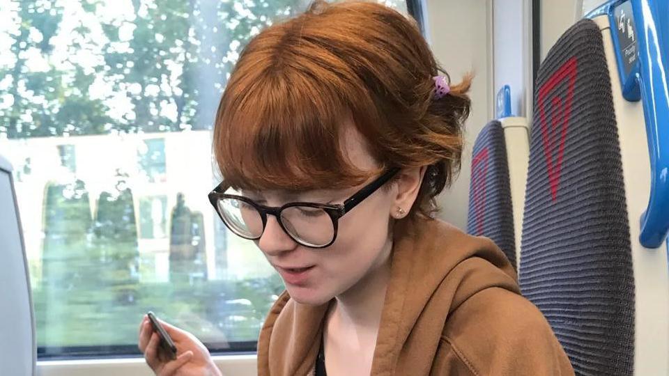 A young woman on the train looking down at her lap. Image source, Clare Rogers