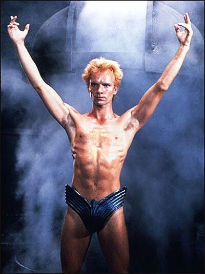 Photo of Sting from the original "Dune" film, striking a triumphant pose while wearing only a tiny pair of metal underpants.