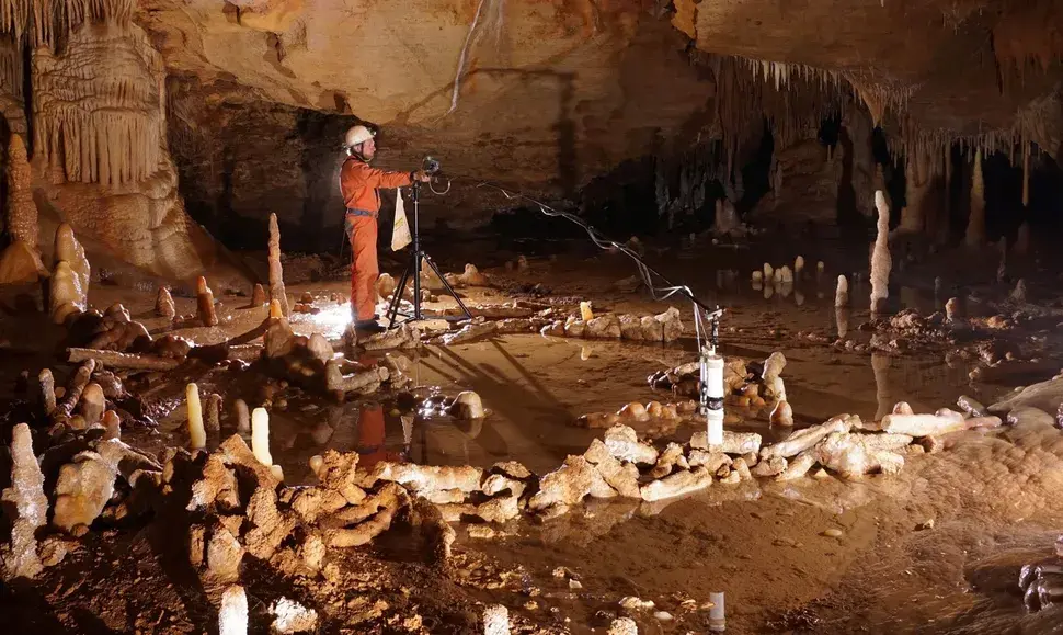 person standing in large well lit cave in the centre of a circle of broken stalagmites